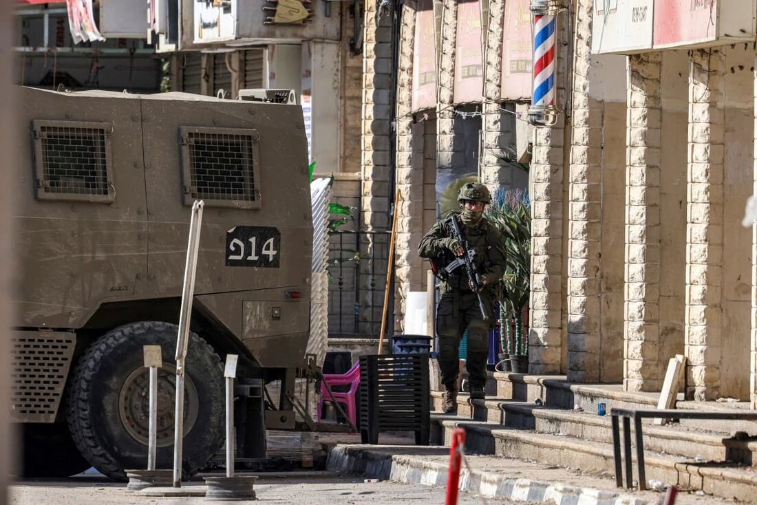 Um soldado israelense passa por lojas ao longo de uma rua durante um ataque do exército ao longo de uma estrada na vila palestina de Qabatiyah