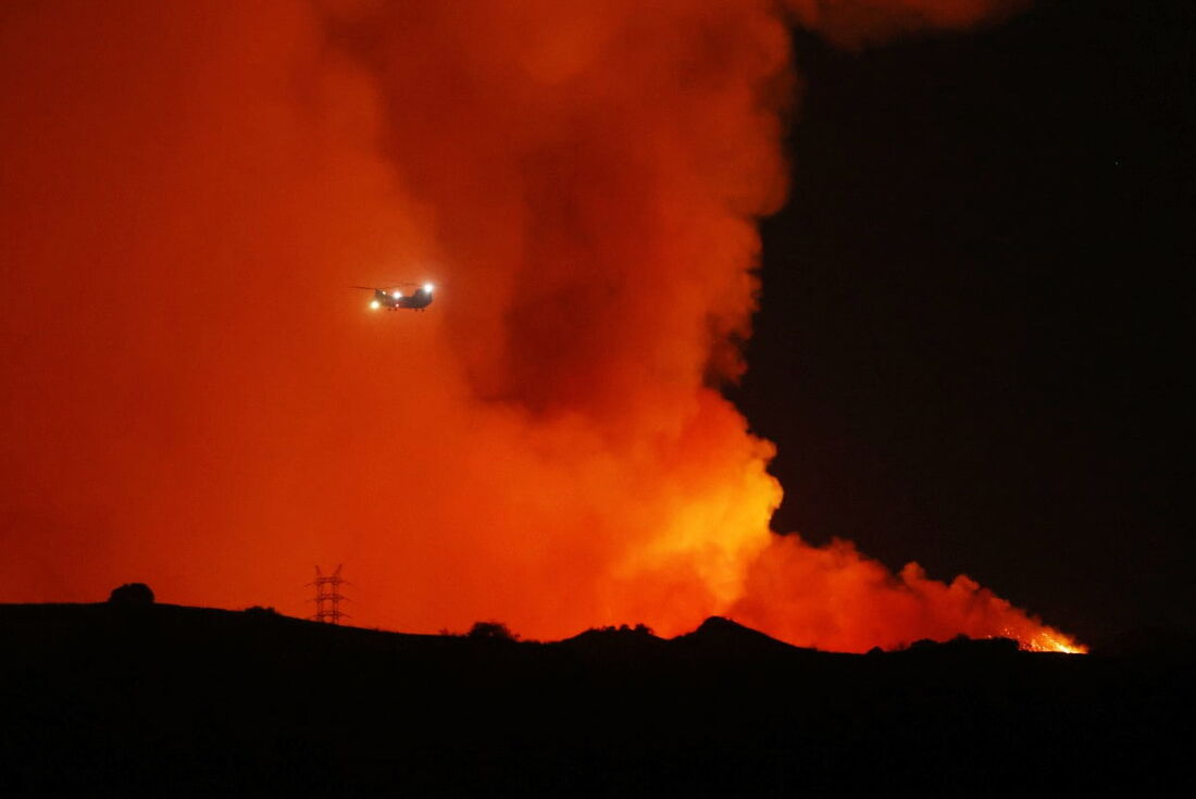 Um helicóptero passa enquanto o incêndio Palisades cresce perto de Encino Hills, Califórnia, em 10 de janeiro de 2025. 