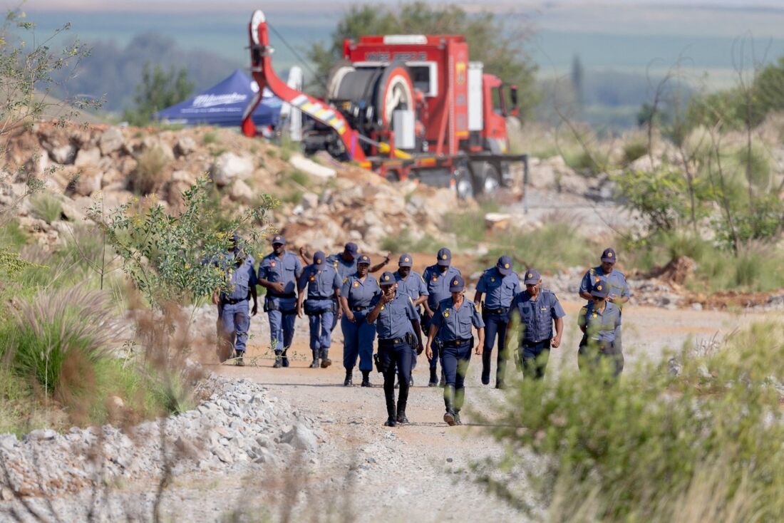 Oficiais do Serviço Policial Sul-Africano (SAPS) caminham perto de um Metalliferous Mobile Rescue Winder durante uma operação de resgate para resgatar mineradores ilegais de um poço de ouro abandonado em Stilfontein