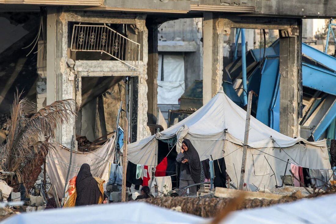 Uma mulher fala ao telefone do lado de fora de uma tenda montada entre os escombros de um prédio destruído em um acampamento para pessoas deslocadas pelo conflito em Bureij, no centro da Faixa de Gaza