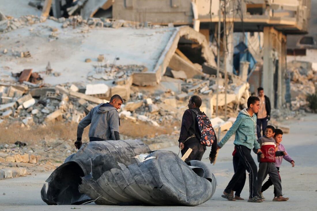 Homens puxam os restos de plástico de uma cisterna destruída ao longo de uma rua perto de prédios desabados em um acampamento para pessoas deslocadas pelo conflito em Bureij, no centro da Faixa de Gaza