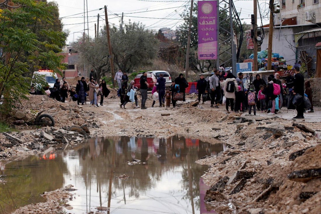 Pessoas carregando seus pertences usam uma rua previamente destruída pelas forças israelenses enquanto fogem do campo de refugiados de Jenin