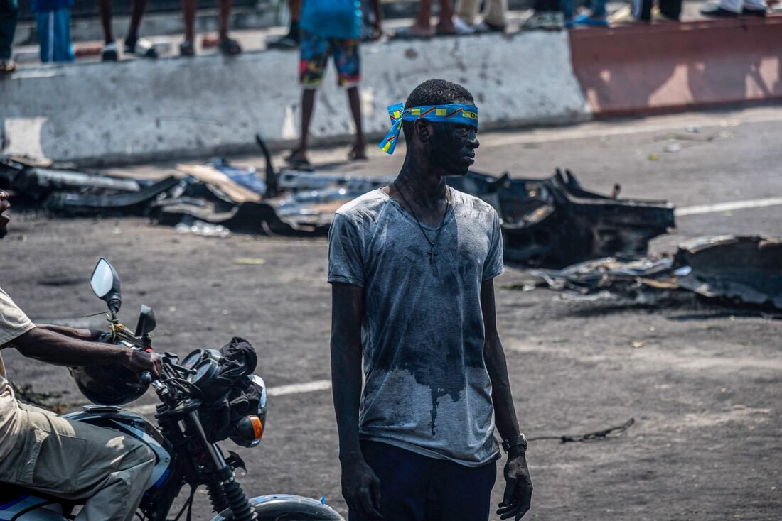 Um manifestante observa, usando uma bandana com a bandeira congolesa na cabeça, em frente aos destroços de veículos queimados e vandalizados durante uma manifestação contra a escalada do conflito no leste da República Democrática do Congo, em Kinshasa, e