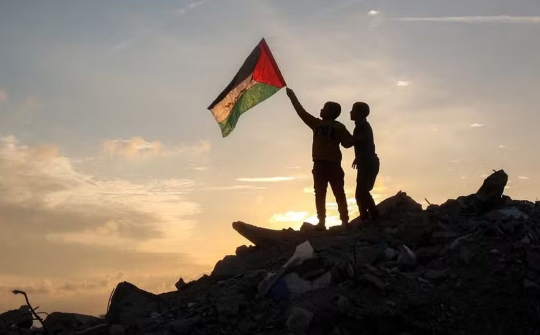 Um menino corre com uma bandeira palestina sobre um monte de escombros em um acampamento para pessoas deslocadas pelo conflito em Bureij, no centro da Faixa de Gaza