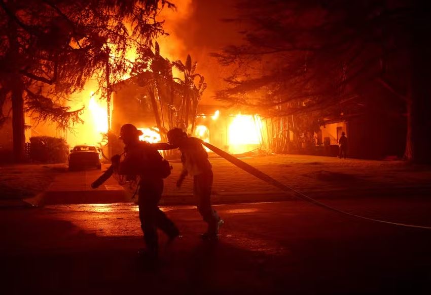 Bombeiros combatem incêndio em frente a uma casa em chamas em Los Angeles, em 8 de janeiro de 2025 