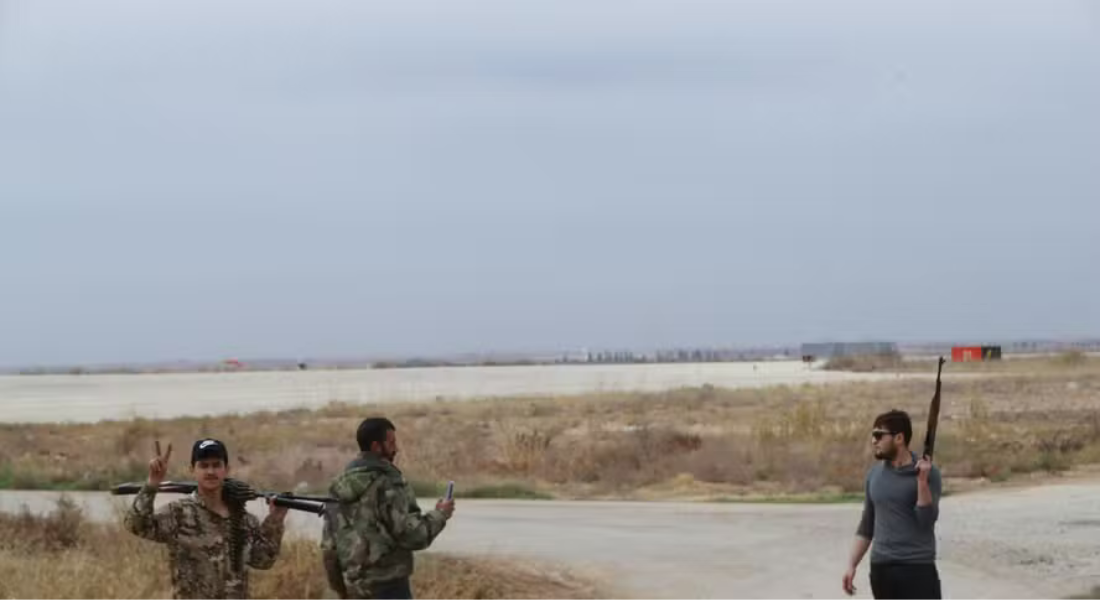 Um combatente curdo sírio exibe o sinal V de vitória enquanto homens armados controlam o aeroporto de Qamishli, no nordeste da Síria, em 8 de dezembro, após a queda da capital Damasco para rebeldes