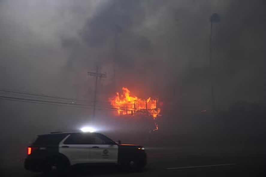 Viatura policial passa por imóvel atingido por fogo em Hollywood Hills, Los Angeles