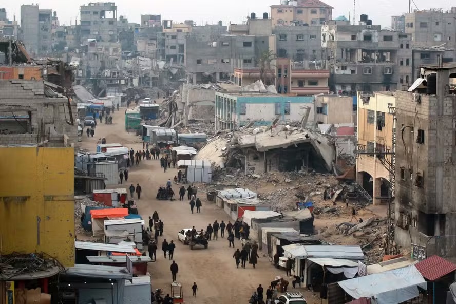 Pessoas passam por barracas que vendem produtos em meio aos escombros de edifícios destruídos durante ataques israelenses anteriores, em Khan Yunis, no sul da Faixa de Gaza 