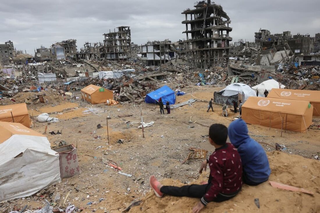 Crianças palestinas deslocadas olhando para tendas montadas em meio a edifícios destruídos em Jabalia, no norte da Faixa de Gaza
