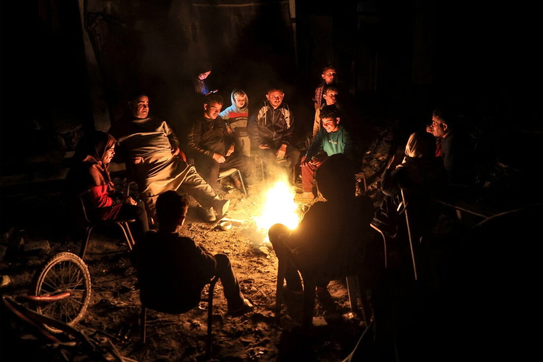 Palestinos sentados perto de uma fogueira em meio às ruínas de suas casas em Jabalia, na Faixa de Gaza
