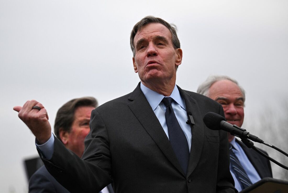 O senador dos EUA Mark Warner, democrata da Virgínia, fala enquanto as pessoas protestam contra a decisão do governo de fechar virtualmente a Agência dos Estados Unidos para o Desenvolvimento Internacional (USAID) no Capitólio dos EUA em Washington, DC, e