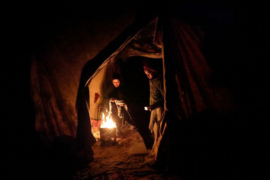 Uma mulher palestina aquece pão no fogo em uma tenda montada em meio às ruínas de edifícios em Jabalia, na Faixa de Gaza