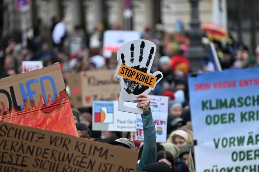 Manifestante segura cartaz com a forma de uma mão onde se lê "Pare o carvão" durante uma "greve pelo clima" convocada por ativistas ambientais do Fridays for Future em fevereiro de 2025 