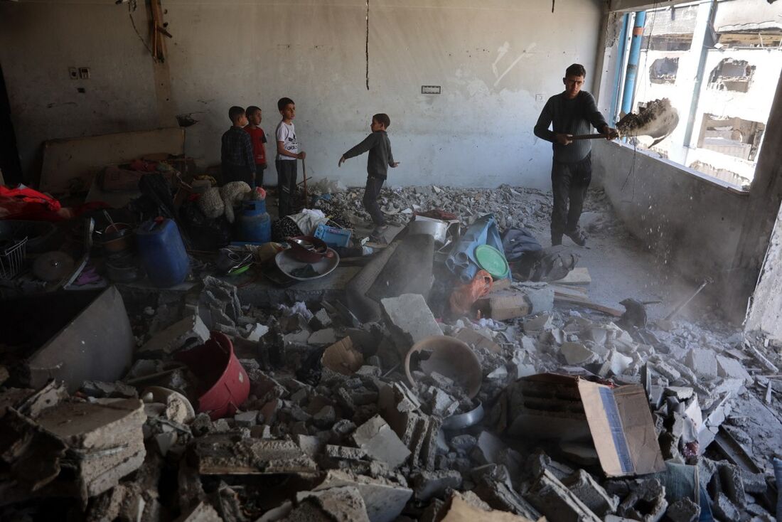 Jovens palestinos limpam escombros dentro de uma sala em um prédio da ONU que abriga uma clínica médica onde palestinos deslocados se abrigaram