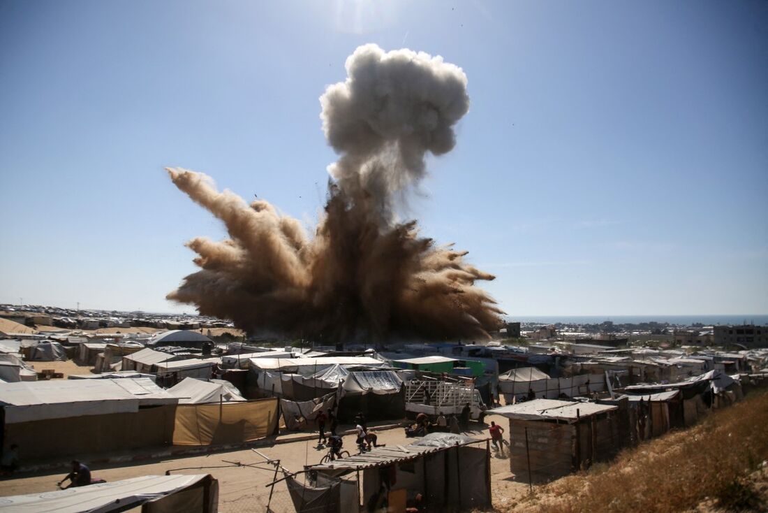 Pessoas correm para se proteger enquanto uma coluna de fumaça sobe acima das tendas em um campo para palestinos deslocados no norte de Khan Yunis, no sul da Faixa de Gaza