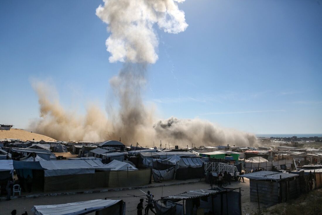 Uma coluna de fumaça sobe acima das tendas em um campo para palestinos deslocados no norte de Khan Yunis, no sul da Faixa de Gaza