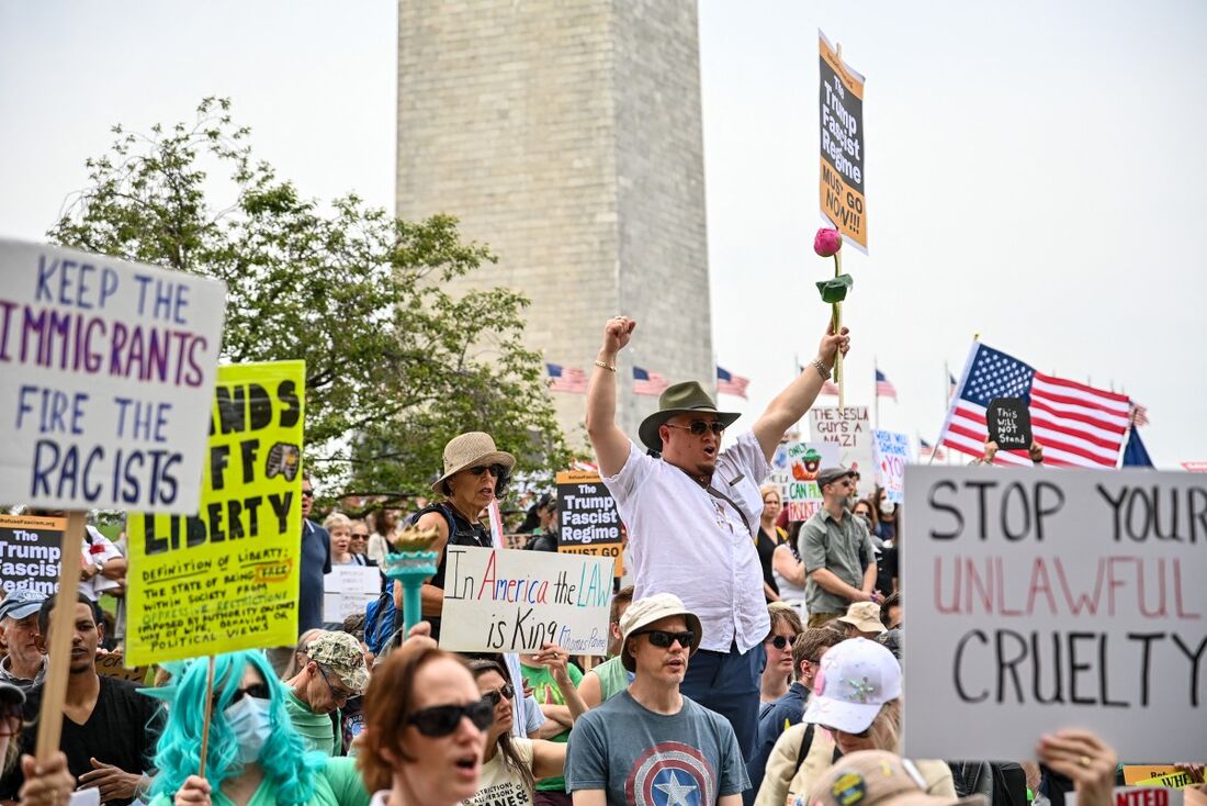 Manifestantes seguram cartazes enquanto marcham em direção à Casa Branca durante um protesto "Free Kilmar Abrego" e um protesto anti-Trump, em Washington, DC