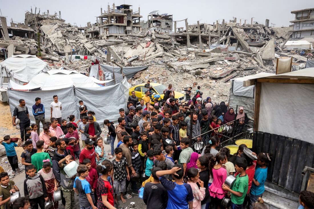 Pessoas fazem fila com panelas para receber refeições de caridade de uma cozinha em Beit Lahia, no norte da Faixa de Gaza