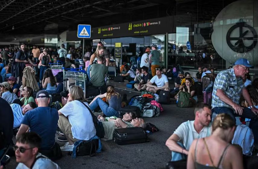 Passageiros com bagagem aguardam do lado de fora do aeroporto Humberto Delgado após apagão geral em Lisboa 