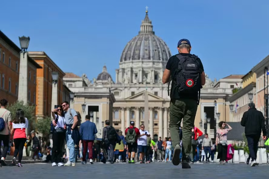 Pedestres caminham pela Via della Conciliazione com a Basílica de São Pedro ao fundo: funeral de Papa Francisco e conclave impactarão na visitação de Roma e Vaticano 