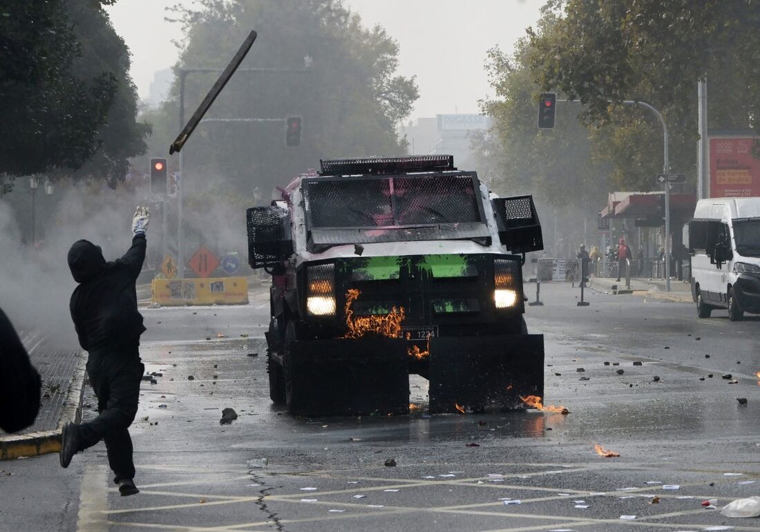 Um manifestante encapuzado atira uma fita de madeira em um carro blindado da polícia de choque durante um protesto do Dia do Trabalho em Santiago, em 1&ordm; de maio de 2025