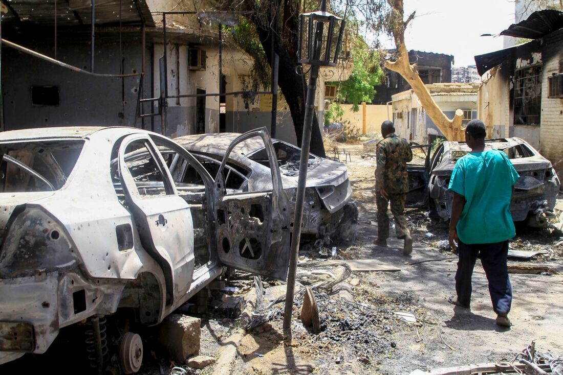 Pessoas passam por veículos destruídos no terreno de um hospital em Cartum, em 28 de abril de 2025. A guerra no Sudão eclodiu em 15 de abril de 2023