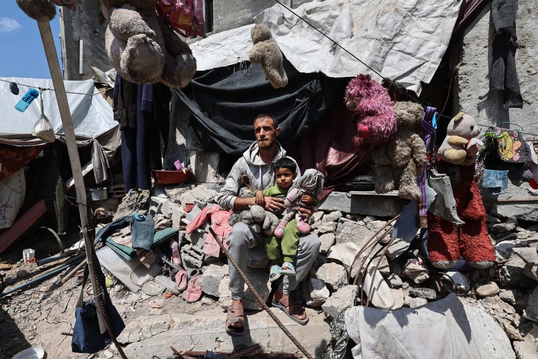 Homem palestino segura criança no colo em meio aos destroços do que sobrou após um ataque de Israel