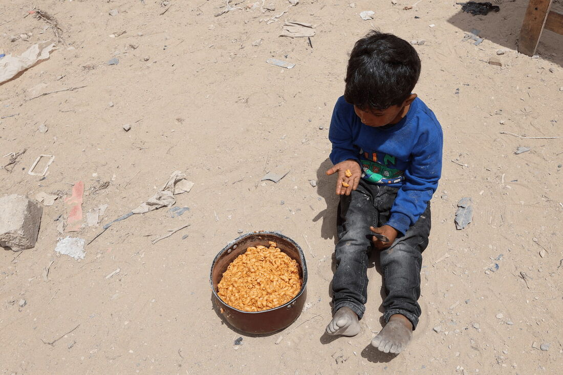 Um menino palestino come um pedaço de uma ração de comida quente de uma cozinha beneficente montada no campus da Universidade Islâmica na Cidade de Gaza