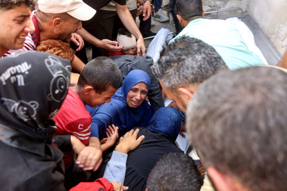 Pessoas sobre os corpos envoltos em manto de parentes mortos em um ataque israelense, no hospital em Gaza