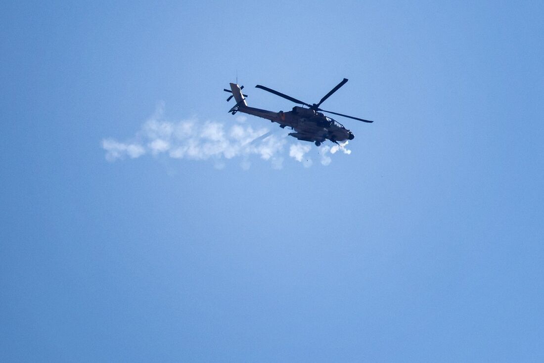 Um helicóptero israelense AH-64 Apache Longbow dispara sua metralhadora perto da fronteira norte de Israel com a Faixa de Gaza