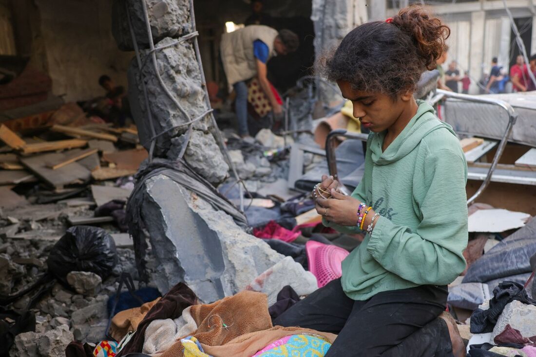 Uma menina recolhe pertences enquanto palestinos verificam o local de um ataque israelense noturno, em Jabalia, no centro da Faixa de Gaza