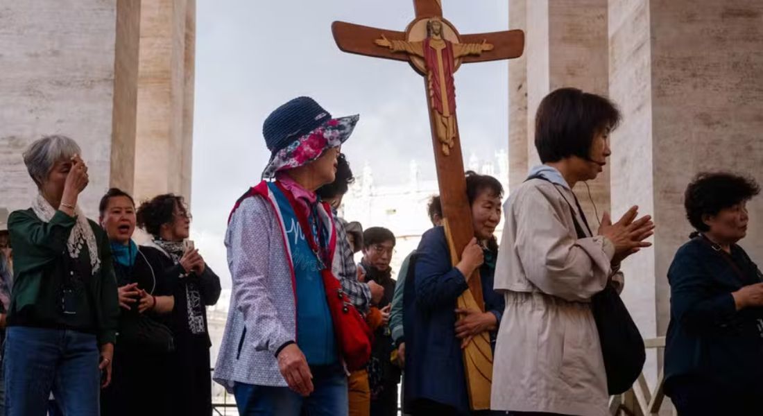 Fiéis caminham com uma cruz um dia antes do início do conclave, no Vaticano