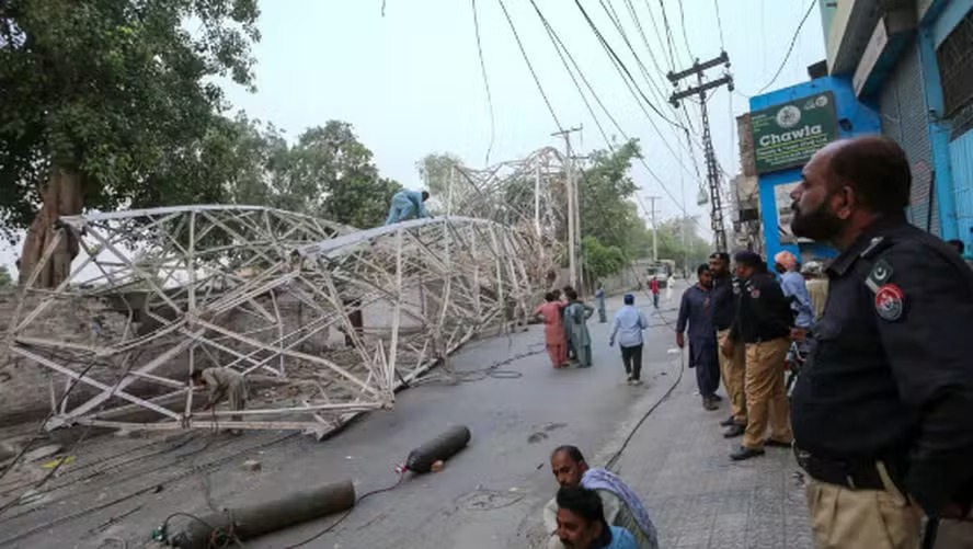 Policial observa enquanto trabalhadores removem uma torre caída após uma violenta tempestade em Multan, Paquistão 