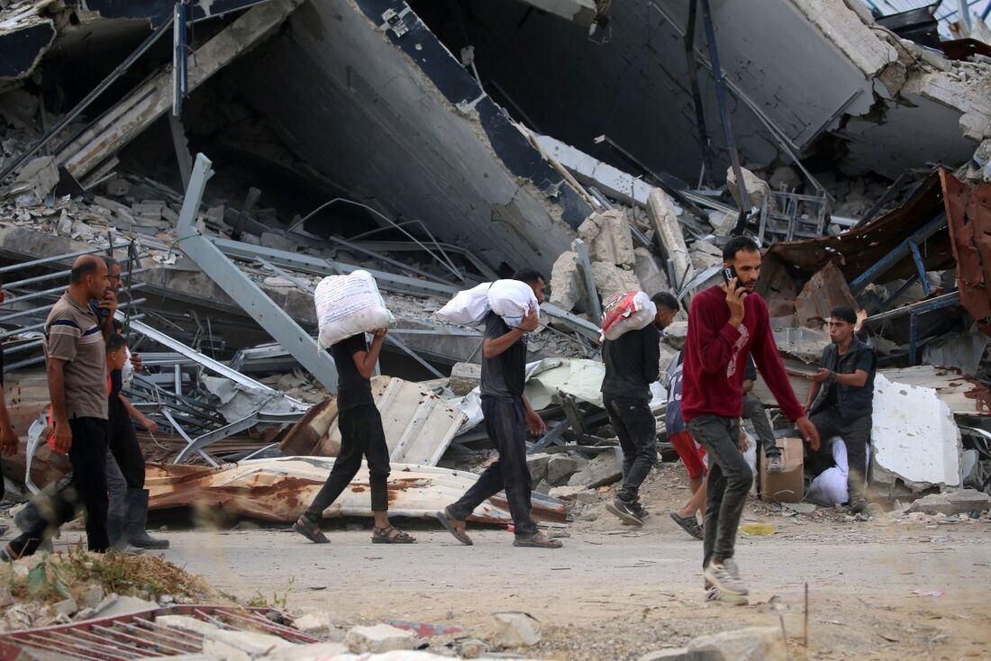Palestinos carregam suprimentos em meio ao cenário de destruição após ataques de Israel