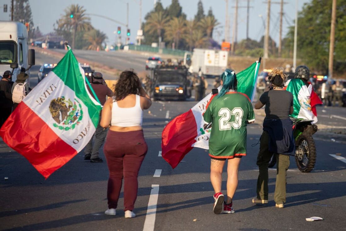 Manifestantes agitam bandeiras mexicanas em frente às autoridades policiais durante um protesto após operações federais de imigração em Los Angeles, Califórnia