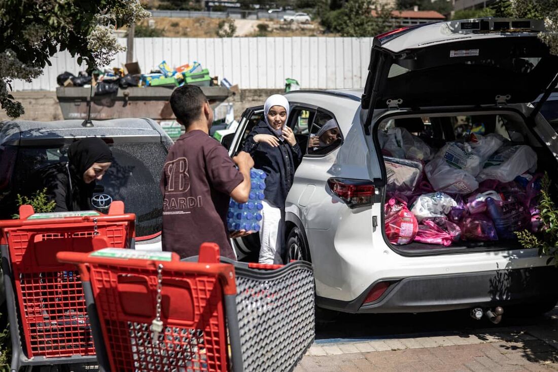 Uma família palestina enche seu carro com produtos comprados, enquanto as pessoas estocam suprimentos em Jerusalém
