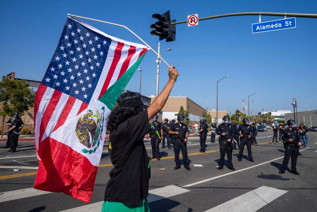 Um manifestante segura uma bandeira combinando as cores das bandeiras dos EUA e do México em meio a confrontos com a polícia nas ruas