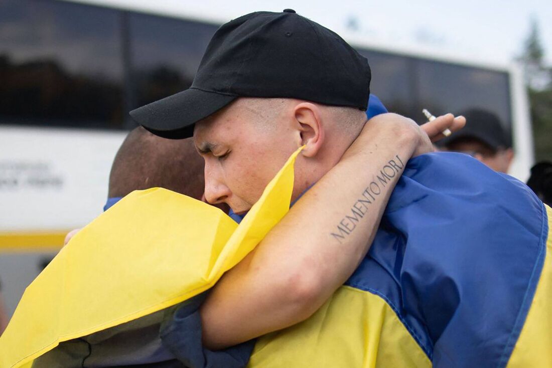 Prisioneiros de guerra ucranianos envoltos em bandeiras nacionais ucranianas se abraçam após uma troca de prisioneiros em um local não revelado, em meio à invasão russa na Ucrânia.