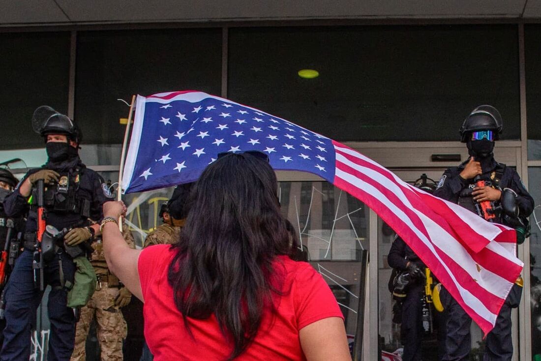 Uma mulher agita uma bandeira dos EUA enquanto membros da Guarda Nacional da Califórnia aguardam do lado de fora do Prédio Federal durante protestos em resposta às operações federais de imigração em Los Angeles