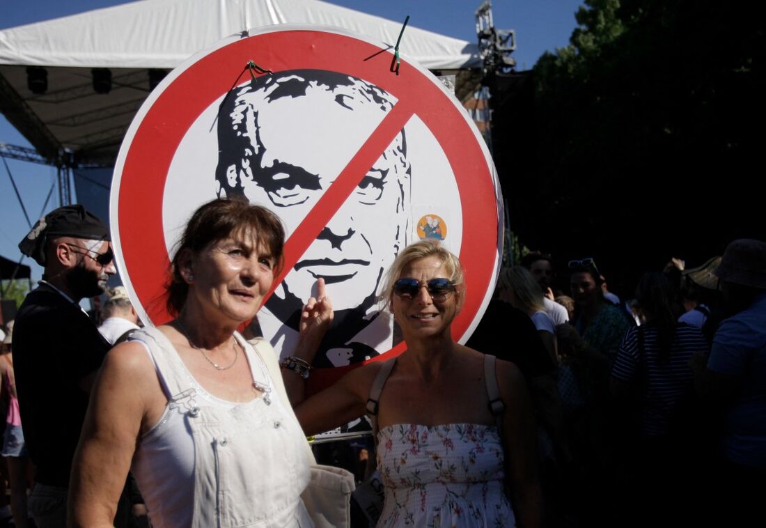 Duas mulheres em frente a uma placa riscando um retrato do primeiro-ministro húngaro, Viktor Orbán, durante a Parada do Orgulho de Budapeste, em 28 de junho de 2025