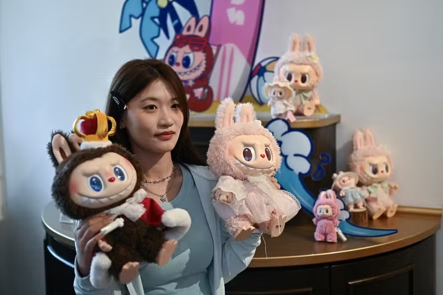 Mulher posando com os personagens Labubu (E) e Mokoko em um salão de exposições enquanto visita o parque temático Pop Land da Pop Mart, em Pequim 