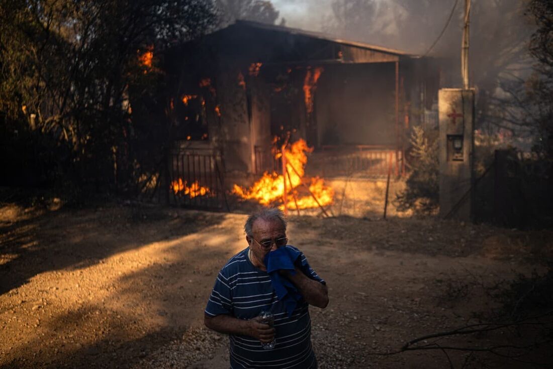 Um homem está em frente a uma casa em chamas durante um incêndio florestal em Pikermi, cerca de 30 km a leste de Atenas