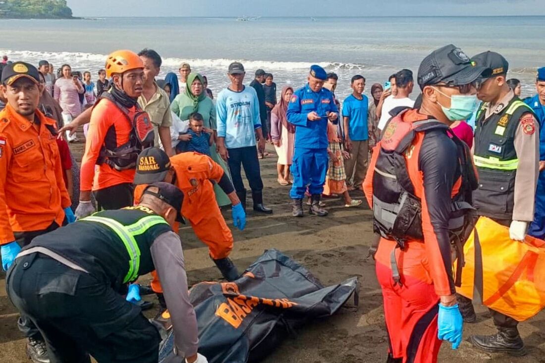Equipe de resgate movendo o corpo de uma vítima trazida para a costa por pescadores locais depois que uma balsa afundou a caminho da ilha turística de Bali