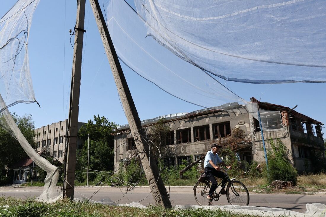 Homem anda de bicicleta próximo a prédios destroçados na Ucrânia