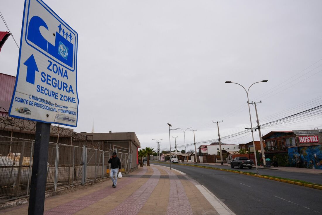 Homem caminha próximo a uma placa de "zona segura" no Chile