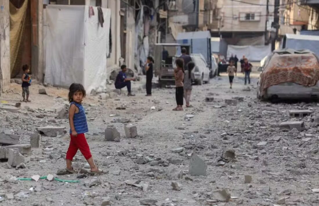 Crianças palestinas caminham em rus coberta por escombros de edifício atingido por ataque israelense na cidade de Gaza 