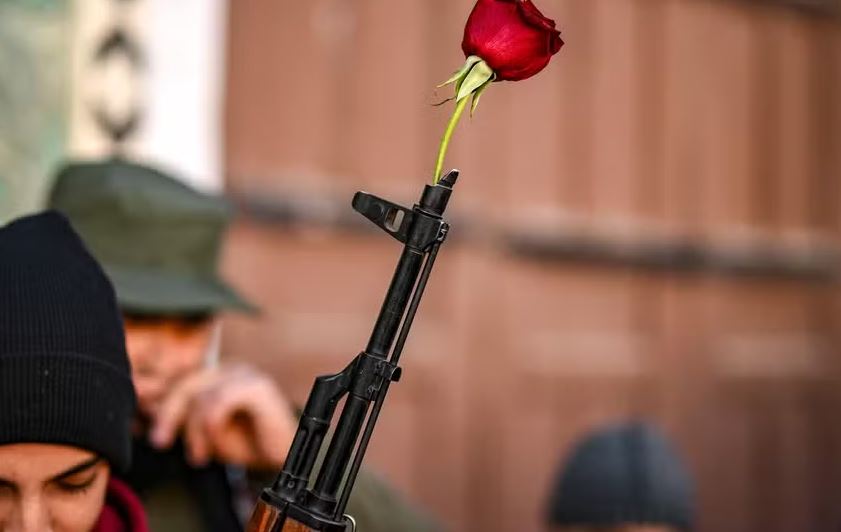 Uma rosa é colocada em um rifle de um combatente rebelde sírio antes das orações semanais muçulmanas de sexta-feira na mesquita Umayyad, em Damasco  Foto: Aris MESSINIS / AFP