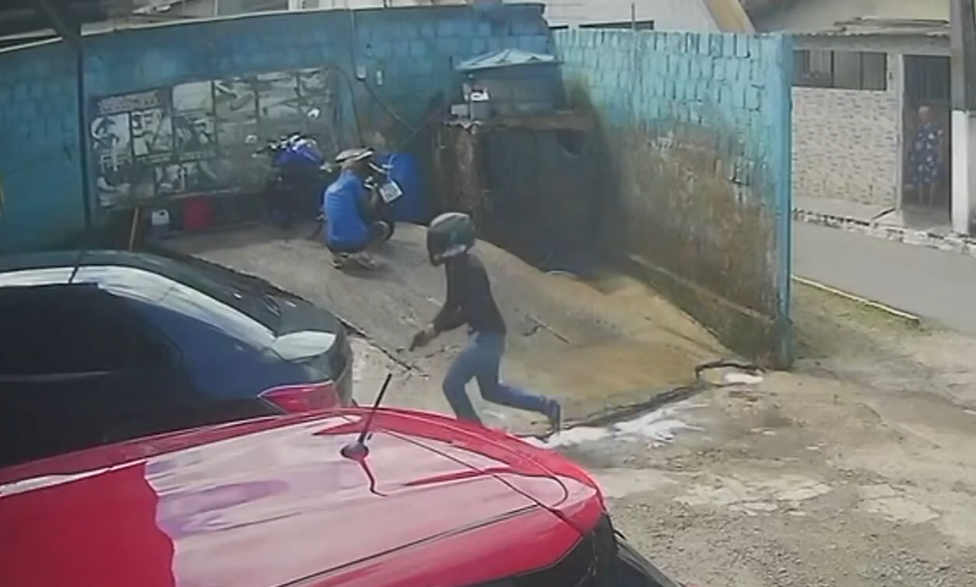 Com uma arma em punho, o homem vai em direção ao jovem, atira e foge em seguida