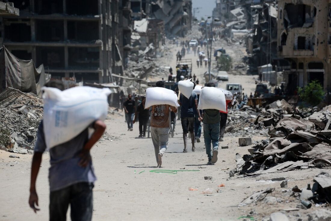 Palestinos carregam sacos de farinha que obtiveram de caminhões de ajuda humanitária que entraram em Gaza pelo posto de fronteira de Zikim, em Jabalia, no norte da Faixa de Gaza.