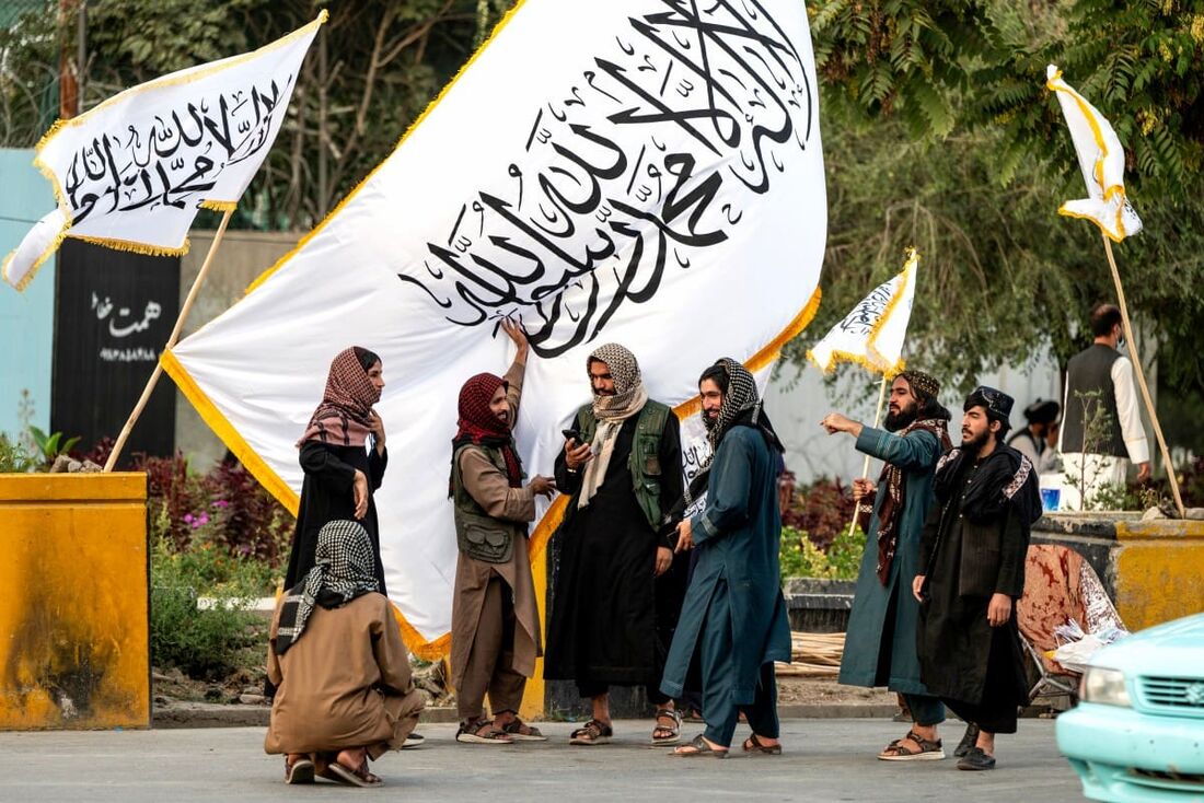 Funcionários do Talibã posam perto de bandeiras do Talibã na véspera do quarto aniversário da tomada do poder pelo Talibã